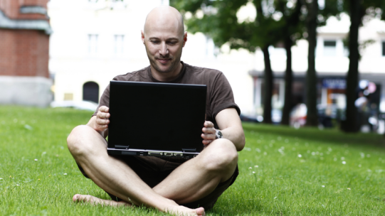 Mann vor Laptop im Rasen